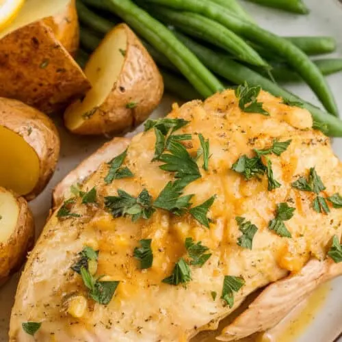 Slow cooker lemon garlic chicken served with roasted potatoes and steamed green beans. The chicken is coated in a rich, buttery lemon garlic sauce and garnished with fresh parsley for a bright and flavorful meal.