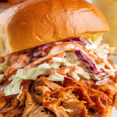 Slow cooker BBQ pulled chicken piled onto a toasted brioche bun, smothered in smoky, tangy sauce, and topped with creamy coleslaw. Served with a side of crispy sweet potato fries for a balanced, flavorful meal.